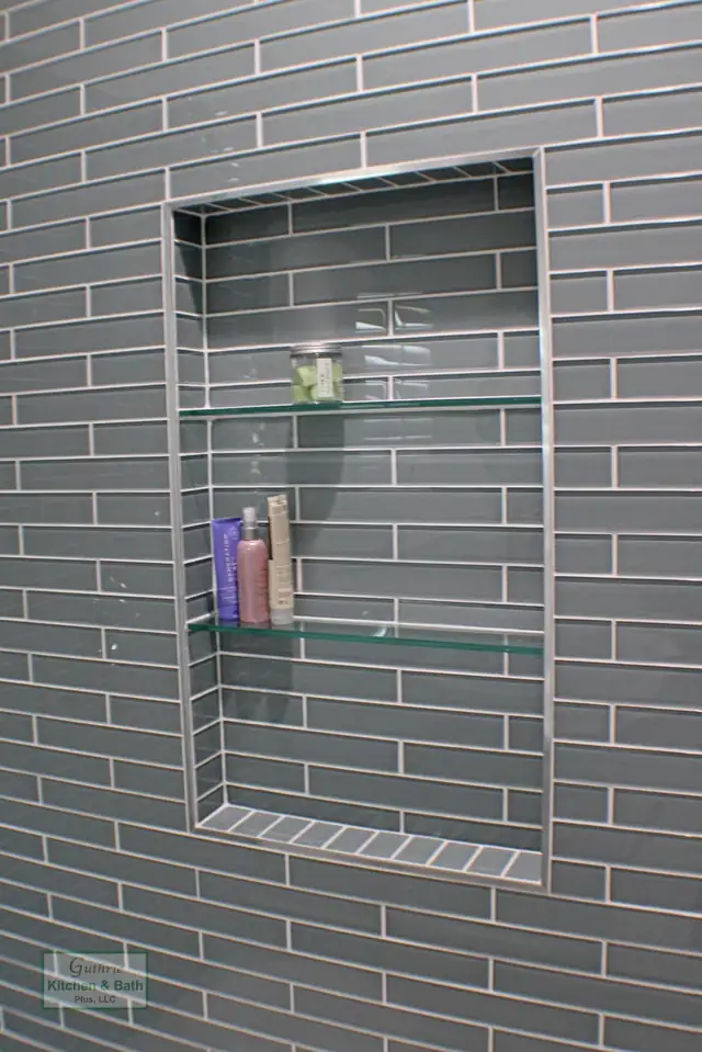 Recessed shower niche with glass shelves set into blue-green glass subway tile in a Springfield, TN bathroom