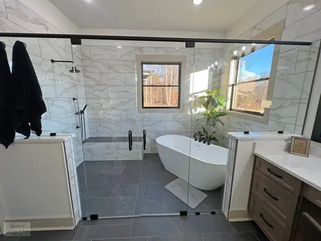 Primary bathroom from a multi-room remodel with white veined tile, a frameless glass shower enclosure, freestanding tub and dark wood vanity