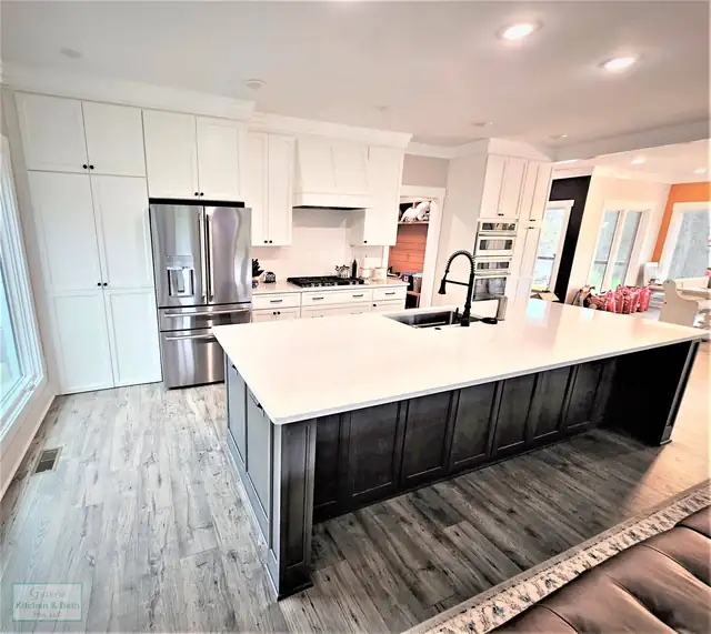 Kitchen remodel with white shaker cabinets, a large white quartz island on a dark base, wood-look floor and stainless appliances