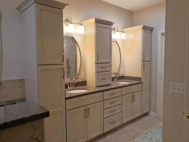 Bathroom with a taupe double vanity, tall linen towers, dark counters and oval mirrors