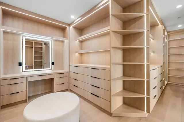 Walk-in closet with light wood shelving, stacked drawers, an illuminated vanity mirror and a built-in seat