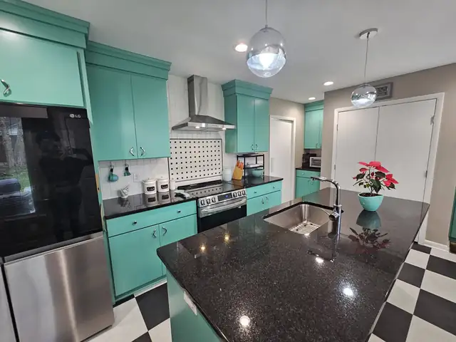 Kitchen with turquoise cabinets, a black granite island with a sink, glass pendants and a checkered floor