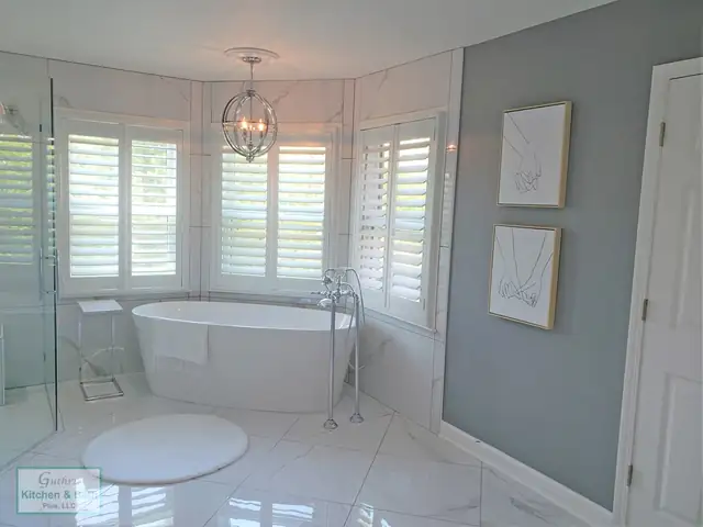 Bathroom with a freestanding tub in a bay window, glass-enclosed shower and marble-look floor tile