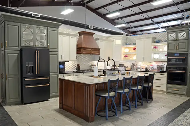 Kitchen display in the Guthrie Kitchen & Bath Plus showroom with sage cabinets, a copper range hood and a stained island