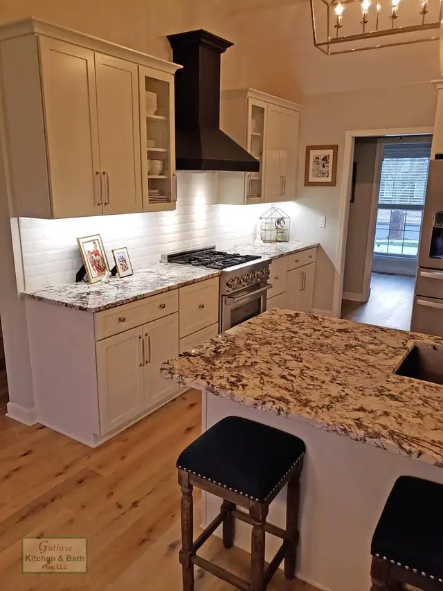 Clarksville, TN kitchen with a speckled granite peninsula, white shaker cabinets, black range hood and navy counter stools